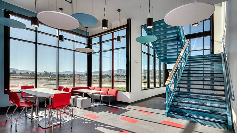 Middle school breakout space and collaboration area with large windows and blue and red accents, including a blue stairway