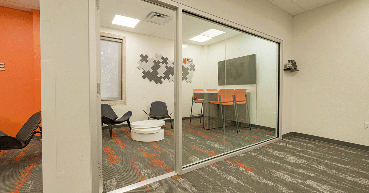 Meeting room within college of business classroom containing rows of desks and chairs and orange accents
